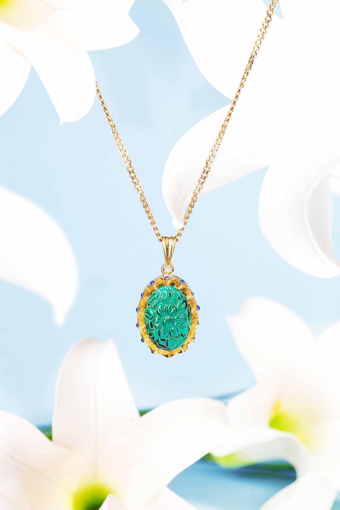 why-choose-us Intricate gold pendant featuring a turquoise gemstone amidst white lilies on a blue background.